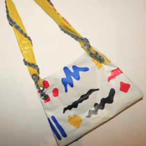 cartera diseñada a partir de pileta infantil rota pvc reutilizado color blanca con dibujos y tira hecha con plástico de descarte amarillo con inscripciones rojas y cordón gris trenzado