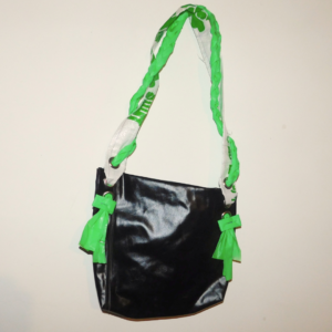 cartera diseñada a partir de colchón inflable pinchado pvc reutilizado color negro con tira hecha con plástico de descarte blanco con inscripciones verdes y trenza hecha de inflable pinchado verde recuperado